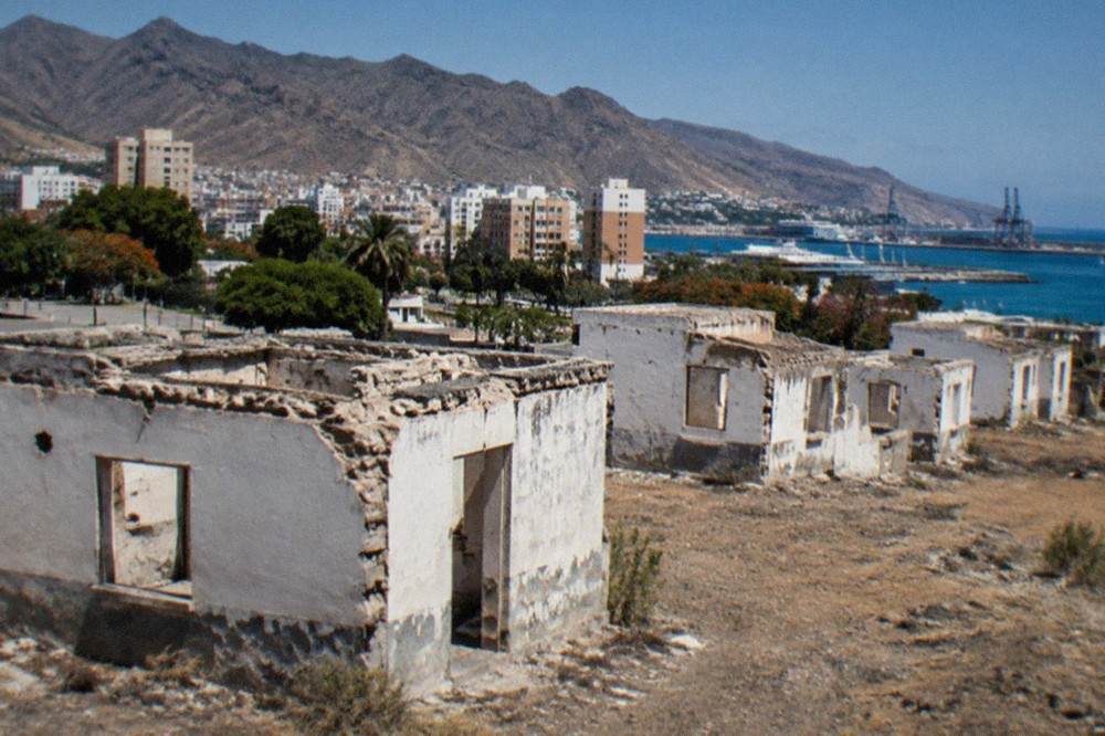 Rows of empty white ruined buildings on dry open ground under a clear sky