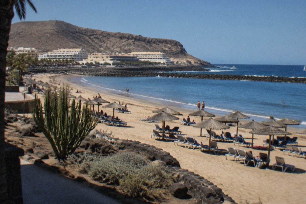 A sunny beach at Playa de las Vistas in Los Cristianos with sunbeds, parasols and calm blue water