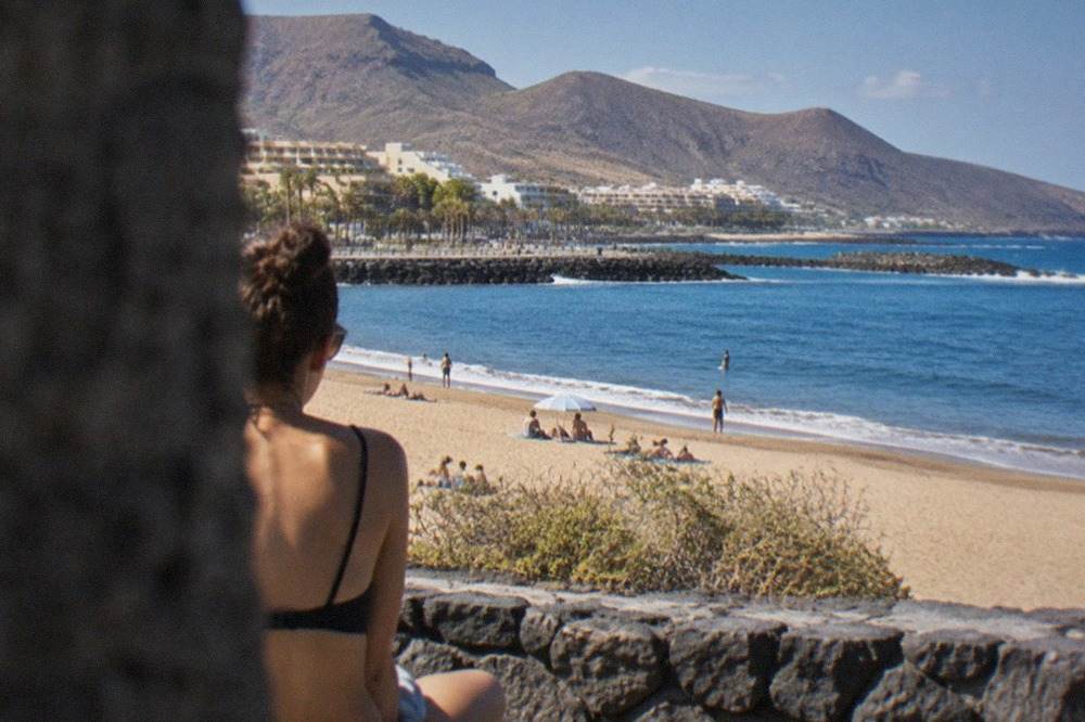 Calm blue sea breaking gently on a sandy Tenerife beach with volcanic hills behind