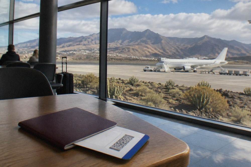 A traveller's passport and boarding pass resting on a table with a view of a Canary Islands coastline in the background