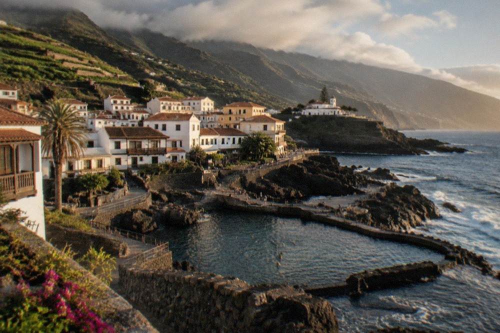 A stone seafront town with natural swimming pools and dark volcanic rock along the waterline in Garachico