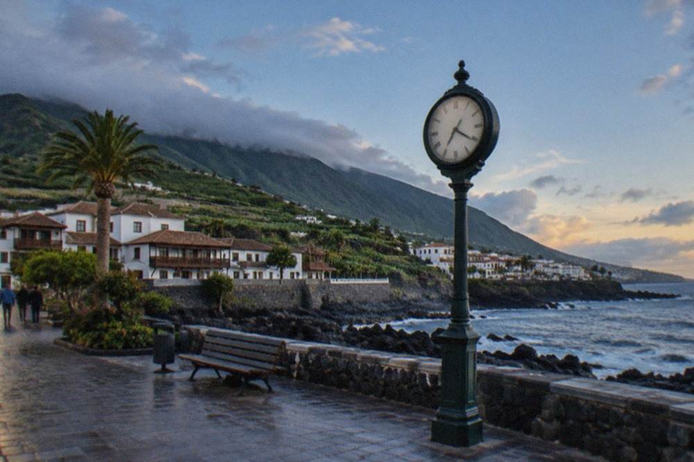 A clock face on a seafront promenade in Tenerife under an evening sky