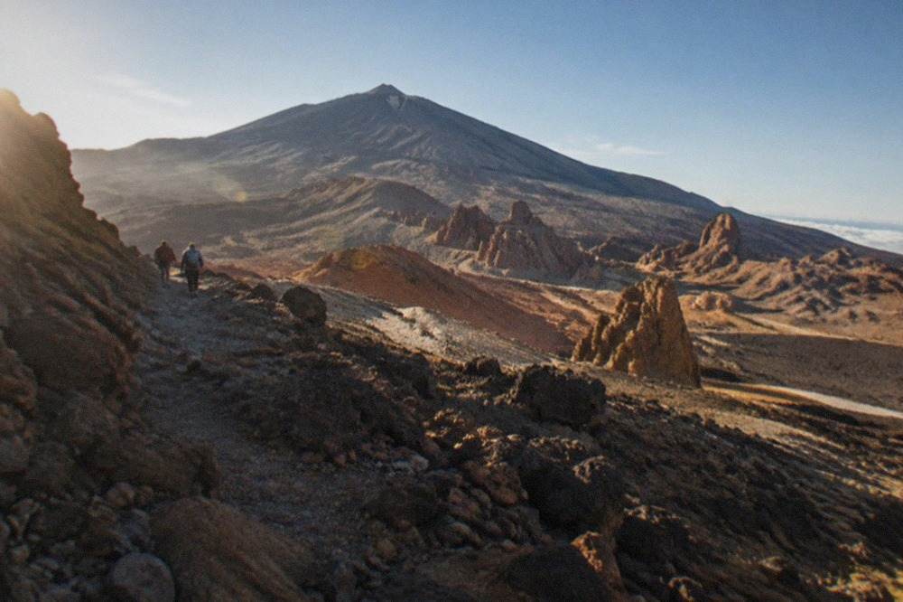 The rocky volcanic slopes of Mount Teide rising above reddish rock formations under a wide sky