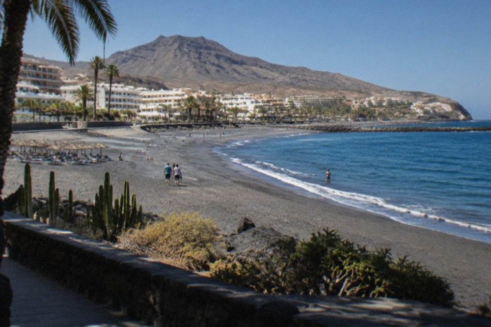 The grey sand beach and hotel frontage of Costa Adeje under a clear sky