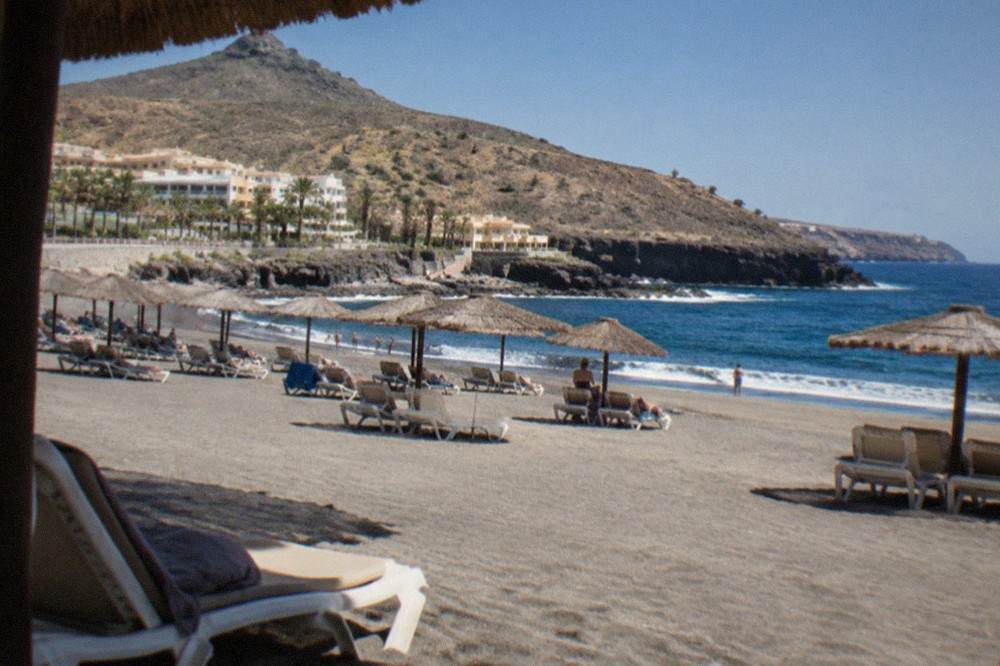Sun loungers and parasols on the grey sand of El Duque beach in Costa Adeje