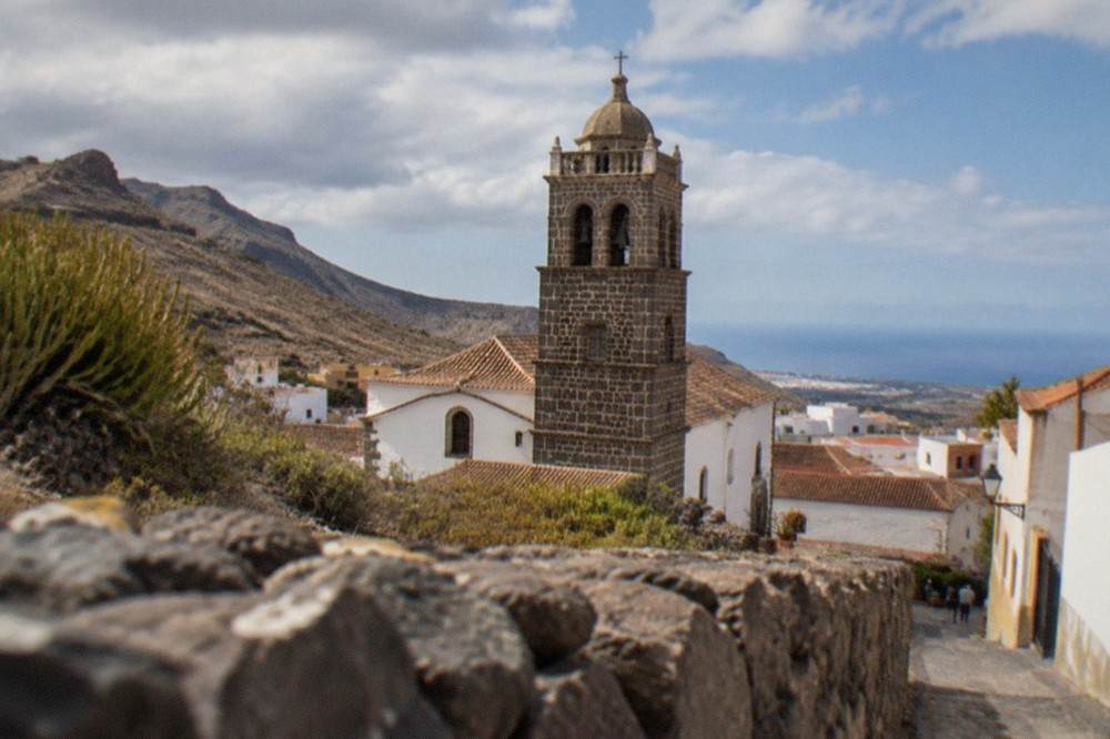 A stone church tower rising above tiled roofs in the centre of Adeje old town