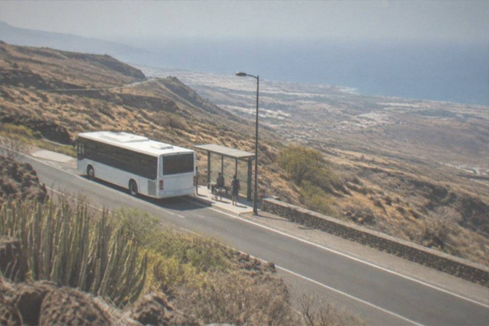 An island bus at a stop on a sunny road above the Adeje coastline