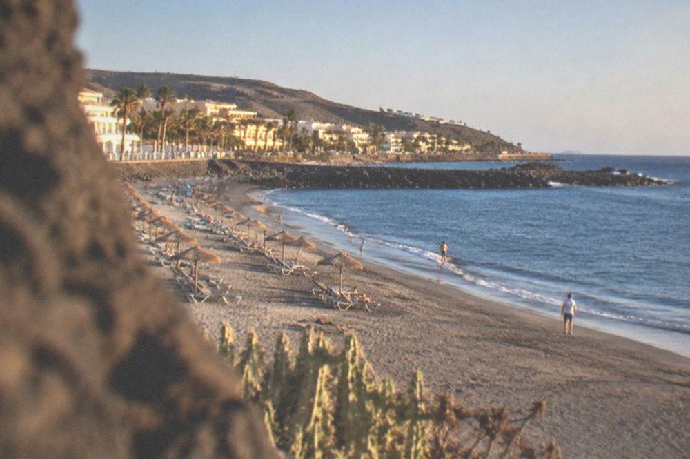 Grey sand beach of Playa del Duque with sunbeds and calm water in Costa Adeje