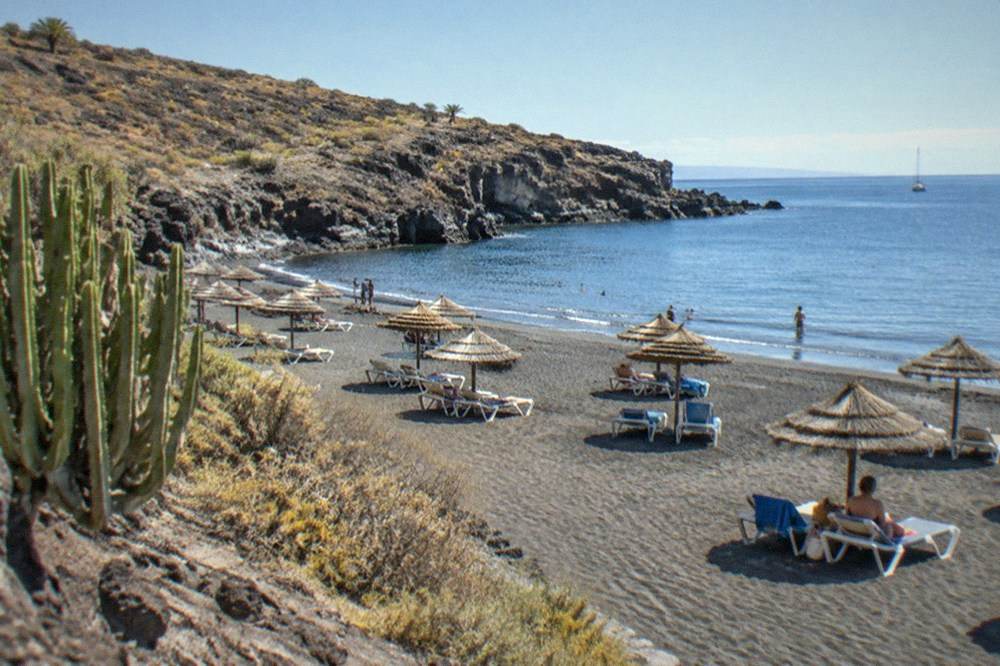 Sunbeds and parasols on a resort beach with calm water in Tenerife