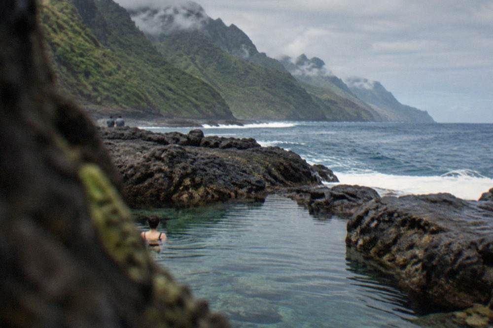 Clear seawater filling a rock pool between dark volcanic ledges on the shoreline