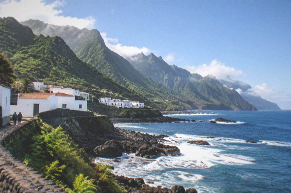 Low white village houses with dark rock walls above a rocky shoreline