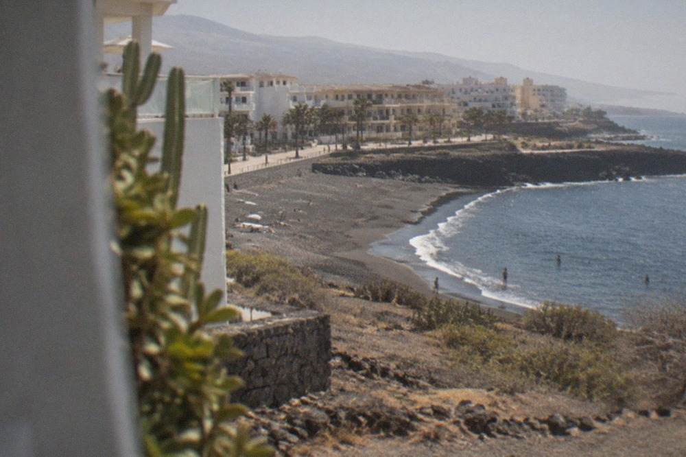 Low-rise white apartment buildings above a small dark-sand bay on a sunny day