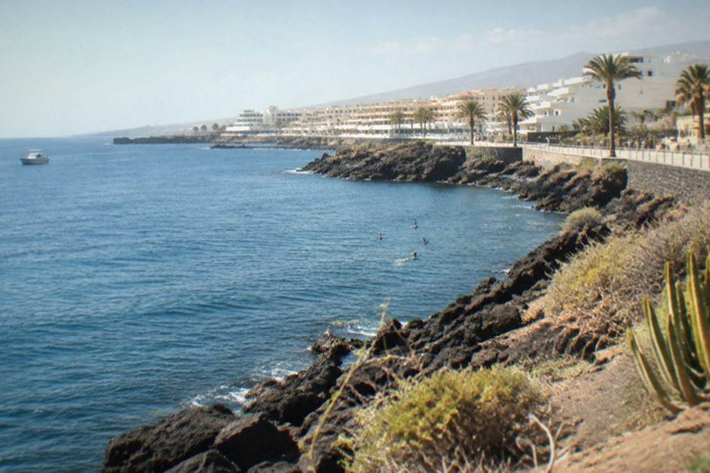 Sunshine on a calm blue sea along a rocky coastline with a few swimmers