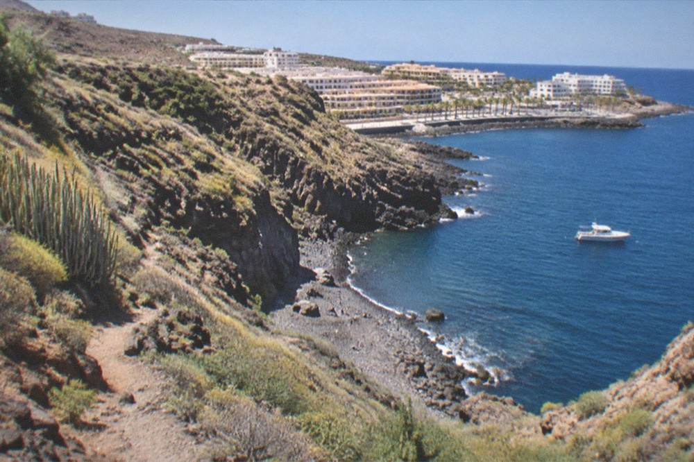 A steep green gorge running down to a small rocky bay with a boat waiting offshore