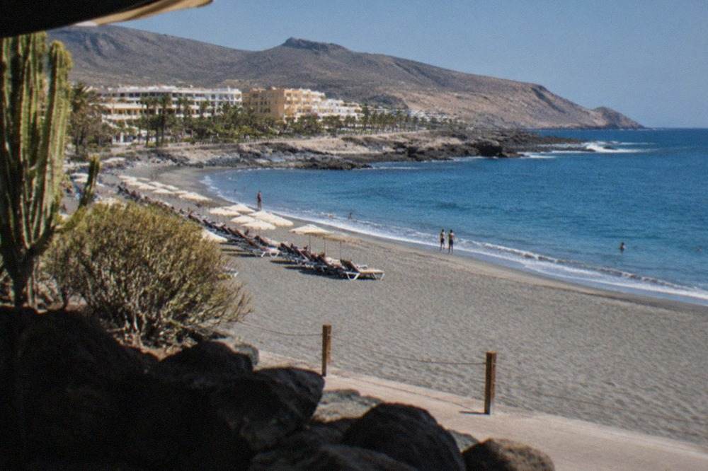 Grey sand beach at El Duque with sunbeds and calm blue water in Costa Adeje
