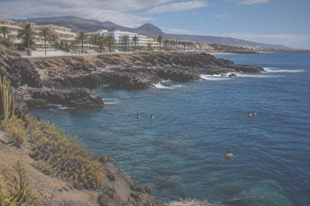 People swimming in clear blue water beside a volcanic rock headland in south Tenerife