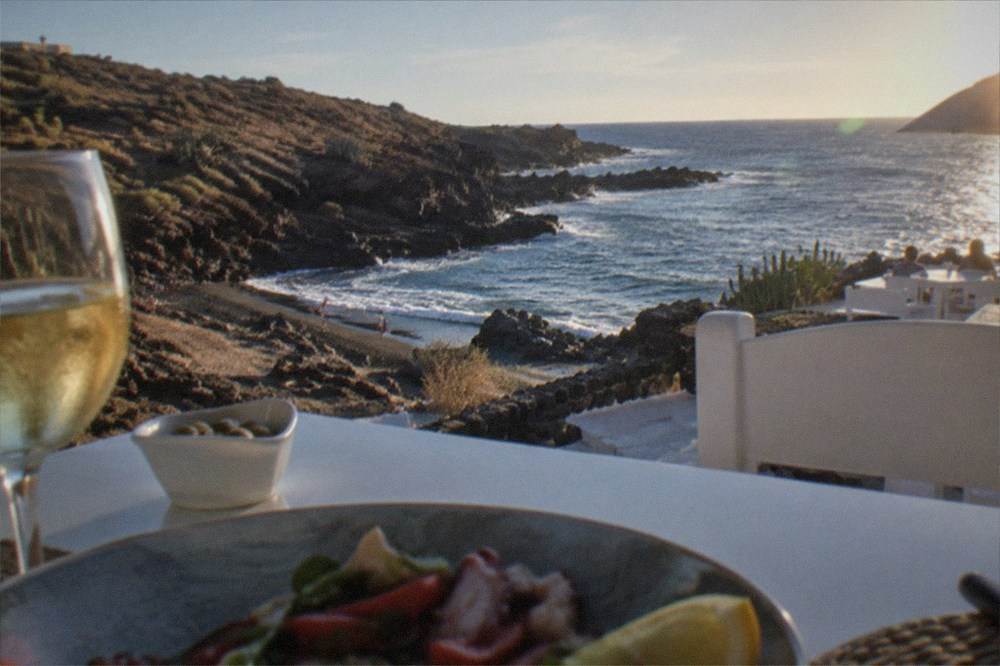 Seafront restaurant terrace with white tables overlooking a small cove at La Caleta