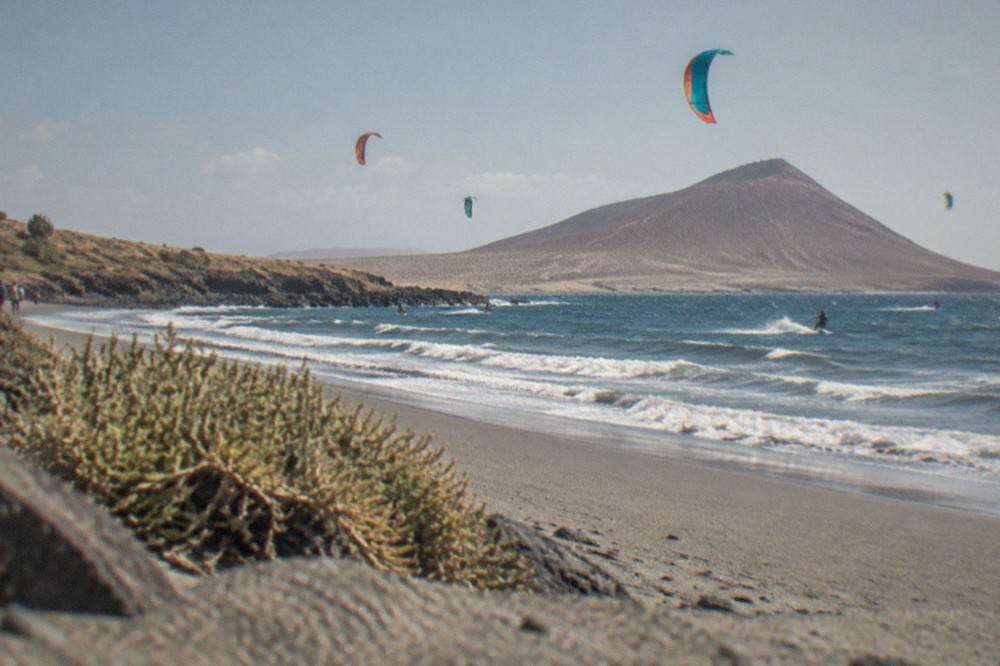 Colourful kite sails over a windy bay with small waves breaking on grey sand