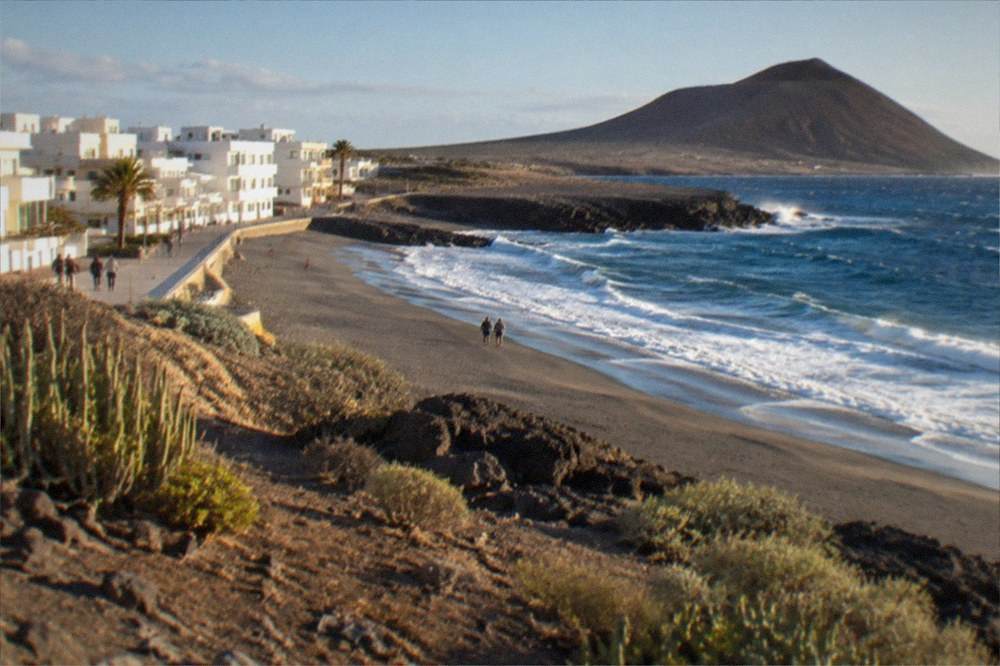Low white apartment buildings beside a promenade facing a windy beach