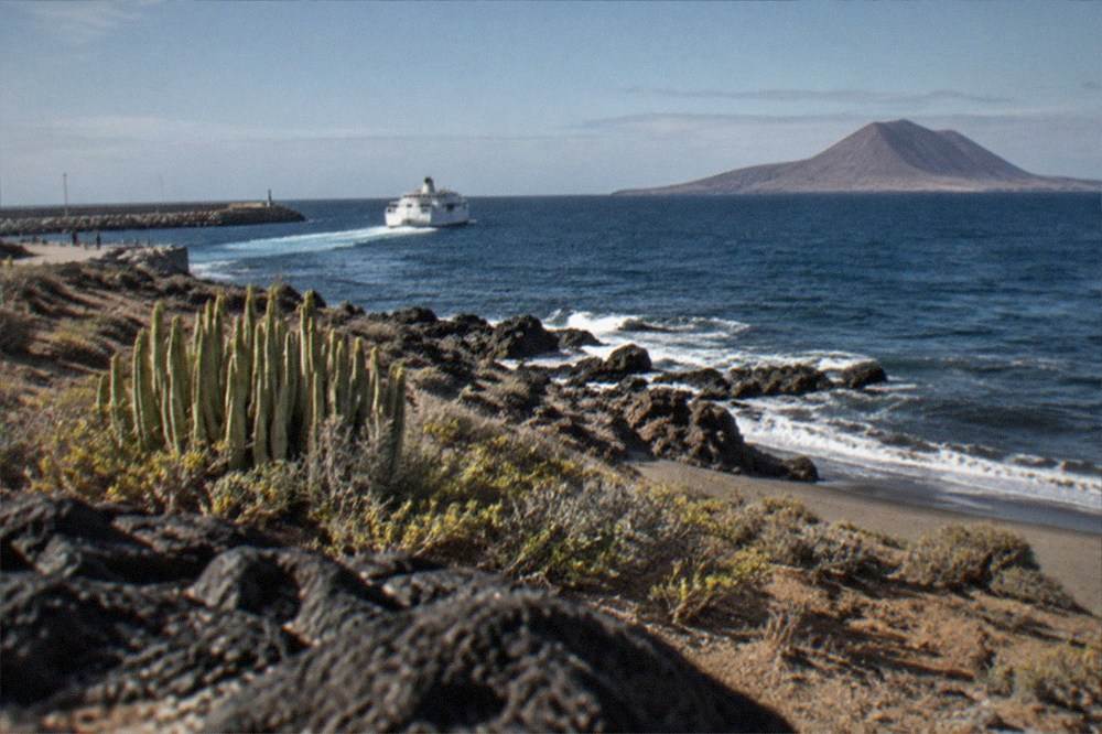 A ferry leaving a southern harbour with a volcanic island on the horizon