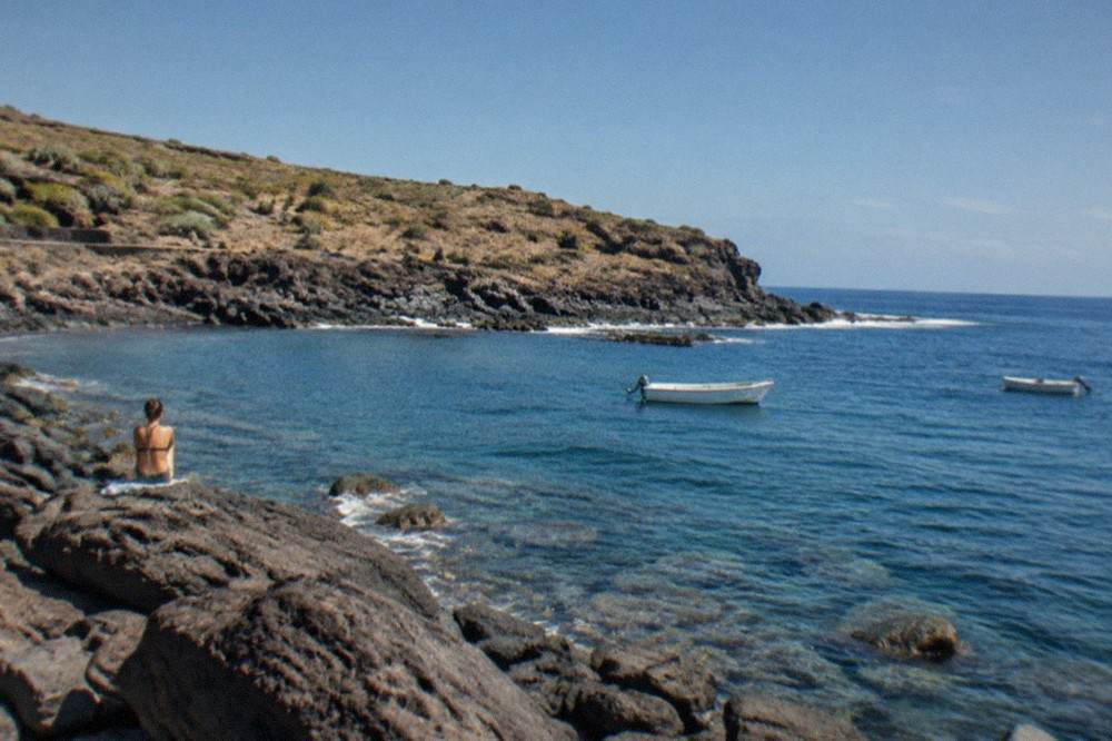 Rocky shoreline beside a calm bay with underwater rocks visible through clear water