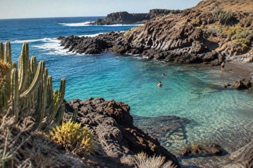 Turquoise shallow water over rocks in a small cove with a rocky point beyond