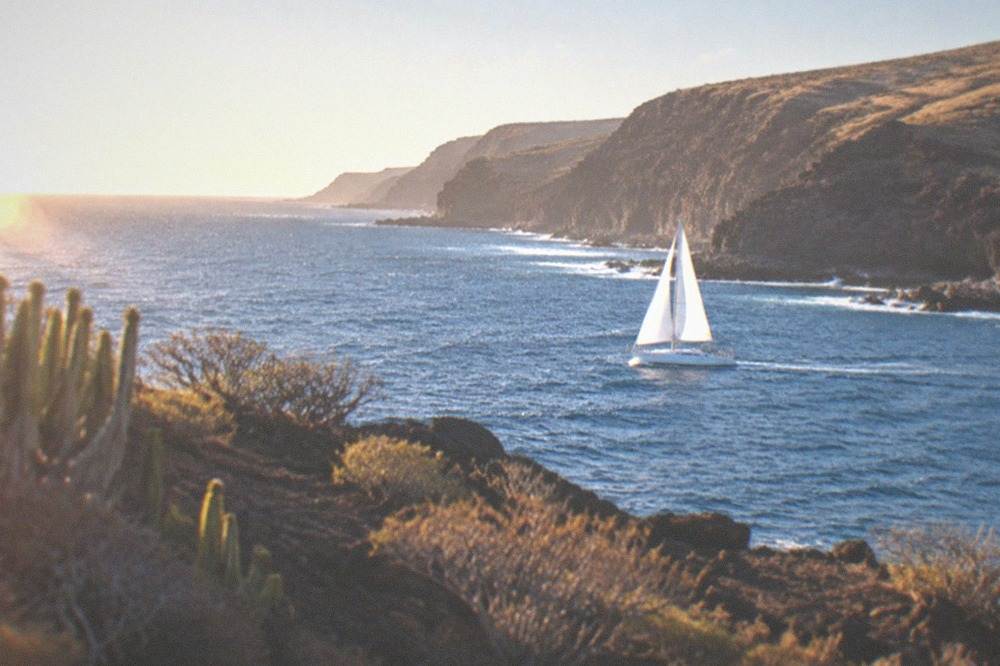 A sailboat passing along a coastline with cliffs and open sea