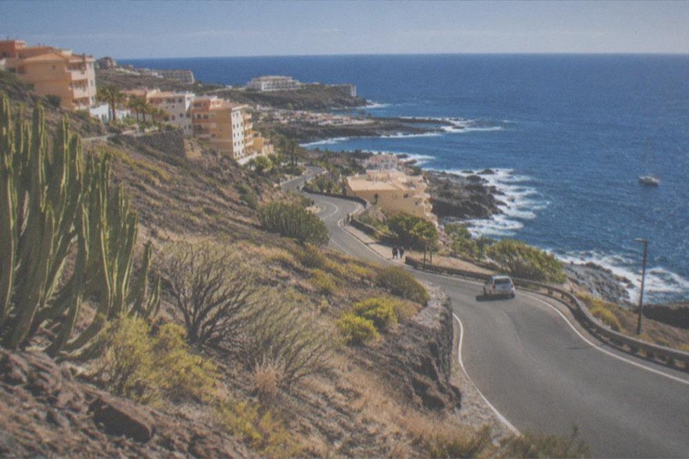 A road winding down toward the coast with apartment buildings on the hillside