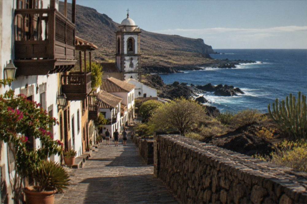 A colonial street with balconied houses and a church tower in an old Canary town