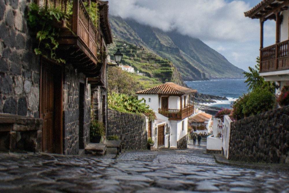 Narrow cobbled street lined with dark stone buildings with wooden balconies in a Canarian town