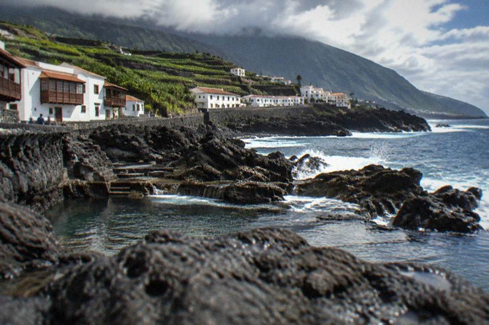 Dark volcanic rock formations at the water's edge with waves washing into natural sea pools