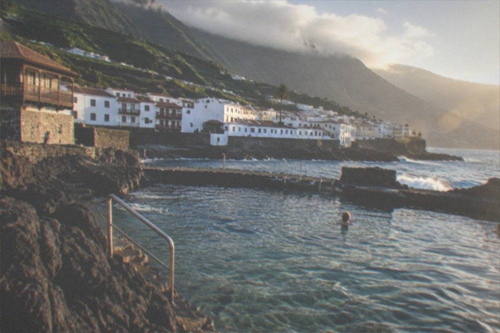 A stone sea pool filled with clear sea water with the town's rooftops behind it