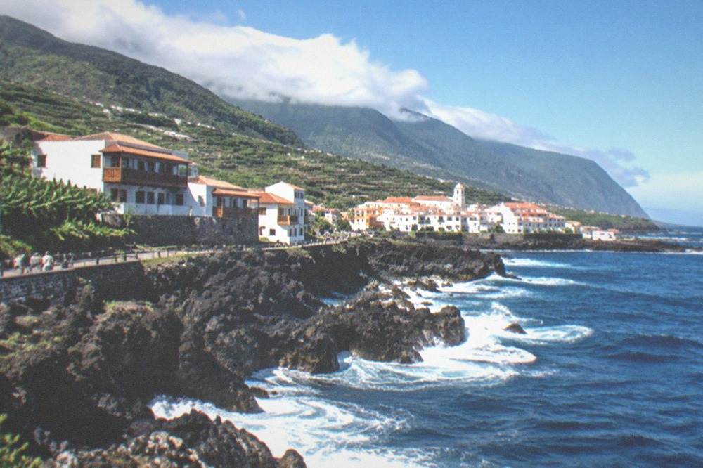Waves breaking against black lava rock below a small Canarian coastal town