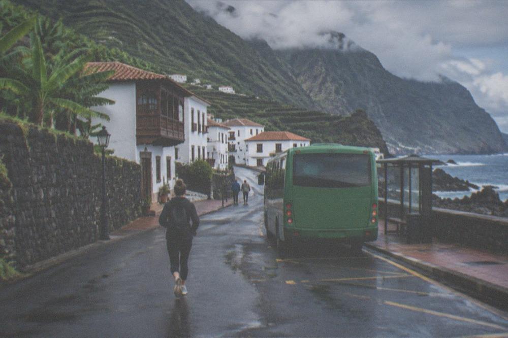 A green island bus at a small town stop with dark rock and sea beyond