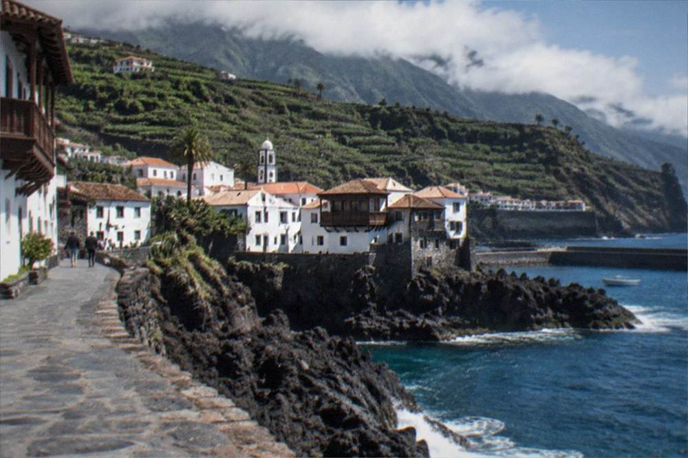 Low clouds resting on green hills above a dark rocky coastline
