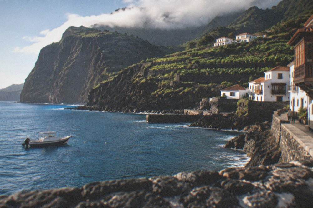 Tall dark sea cliffs rising straight from blue water with a small boat nearby