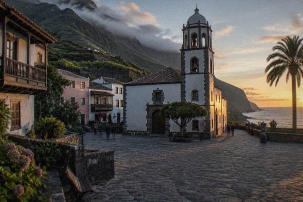 A small town square at dusk with a church tower and pastel facades