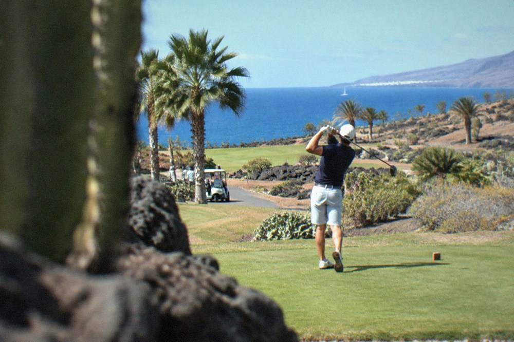Golfer teeing off on a green with palm trees and volcanic rock