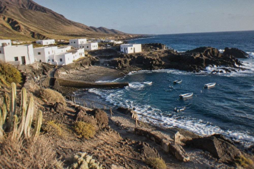 A small coastal village with low white buildings beside a rocky bay on a sunny day in south Tenerife