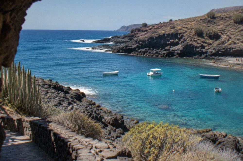Rocky coastline with clear turquoise water and a few small boats moored close to shore