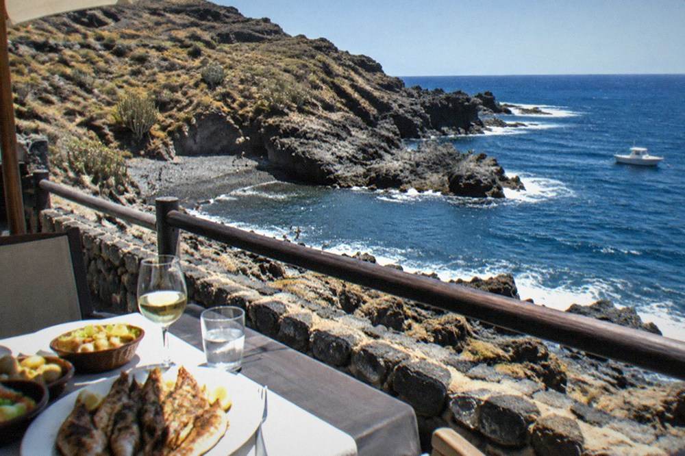 An evening terrace of a seafood restaurant overlooking a small rocky cove