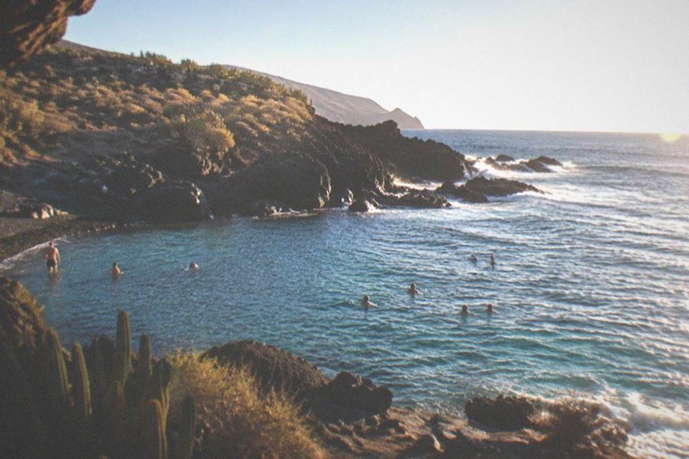 People swimming in a clear rocky cove with sunlight on the water