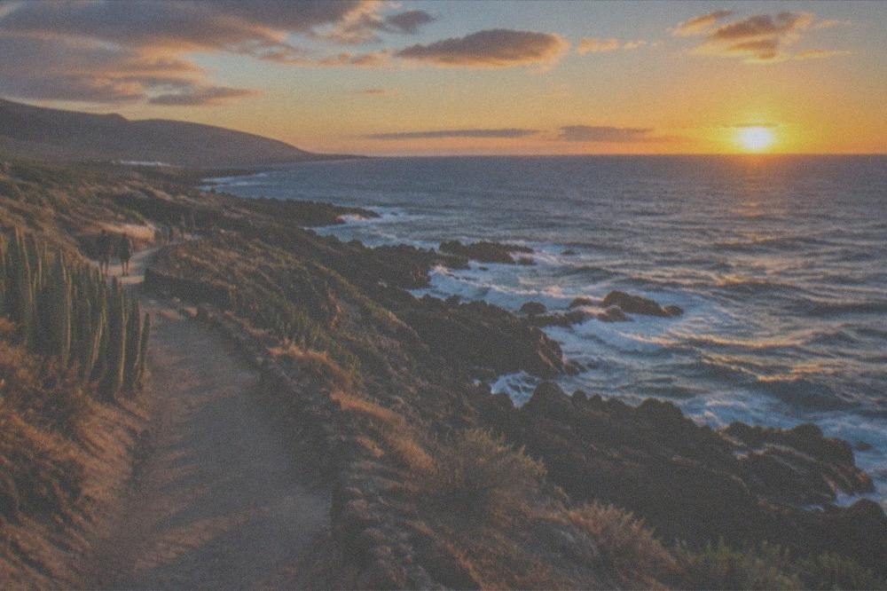 A coastal walking path above rocks with the sunset sky over the sea