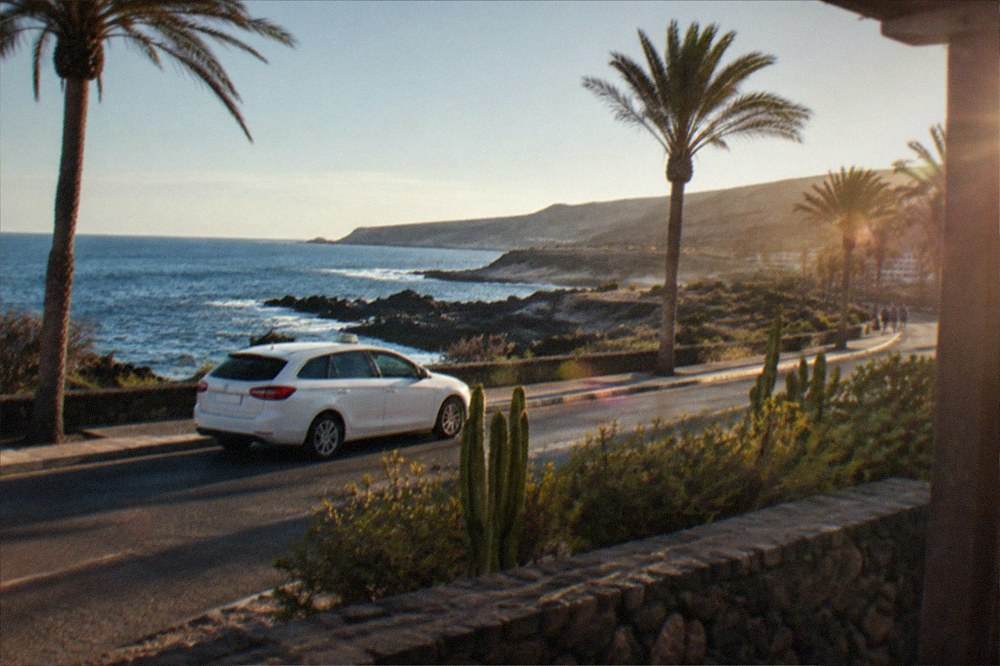 A white taxi and a coastal road with palm trees and low buildings