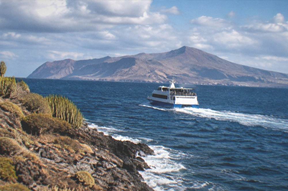 A ferry leaving a harbour towards a mountainous island on the horizon