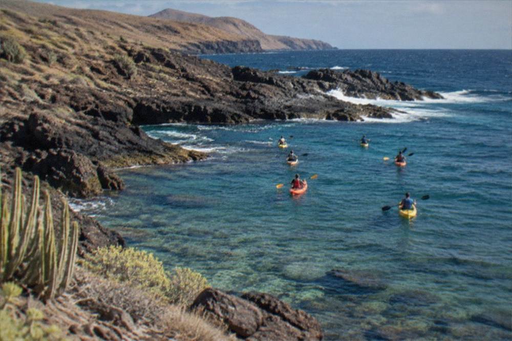 A kayak group paddling over clear shallow water near volcanic rocks