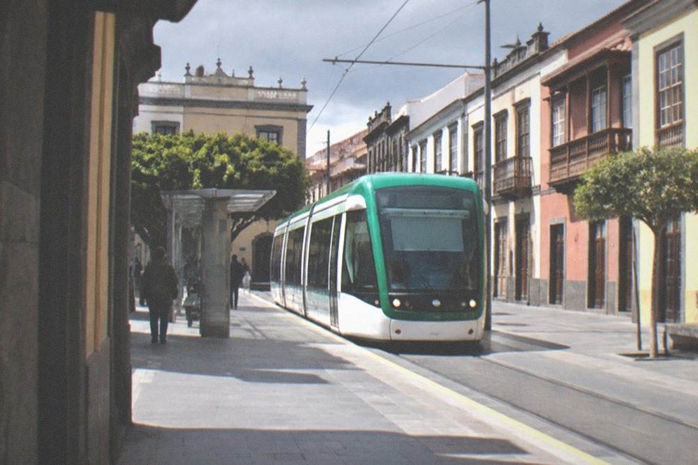 A green and white tram arriving at a stop in La Laguna