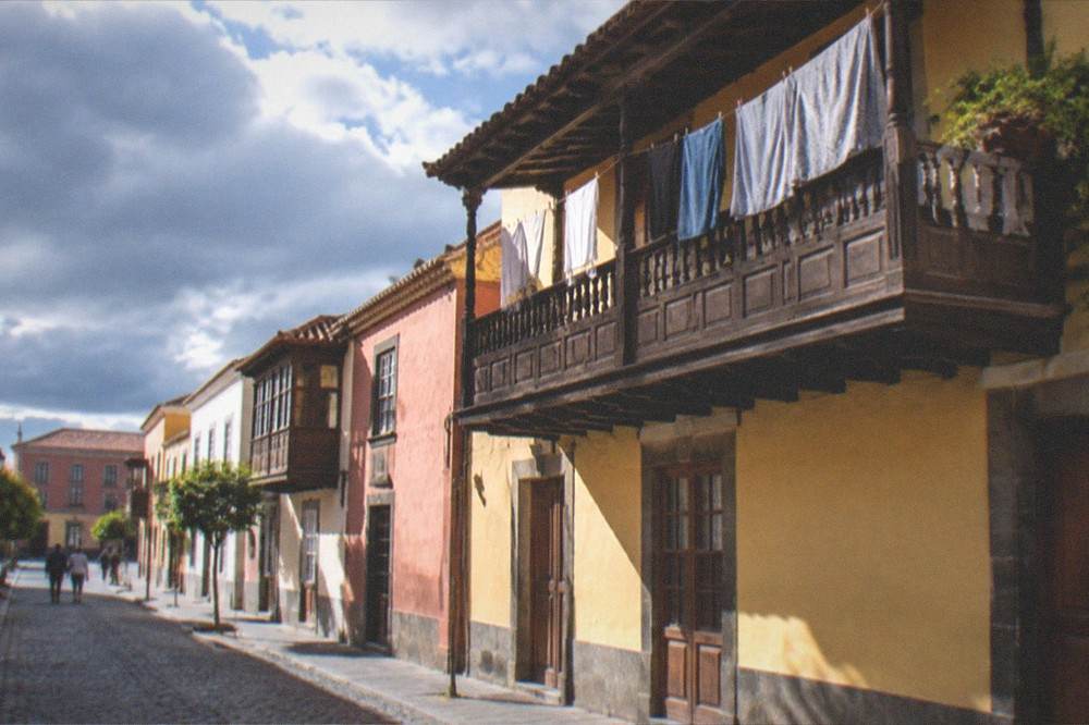 Sunlight on a cobbled street with laundry above a wooden balcony in La Laguna