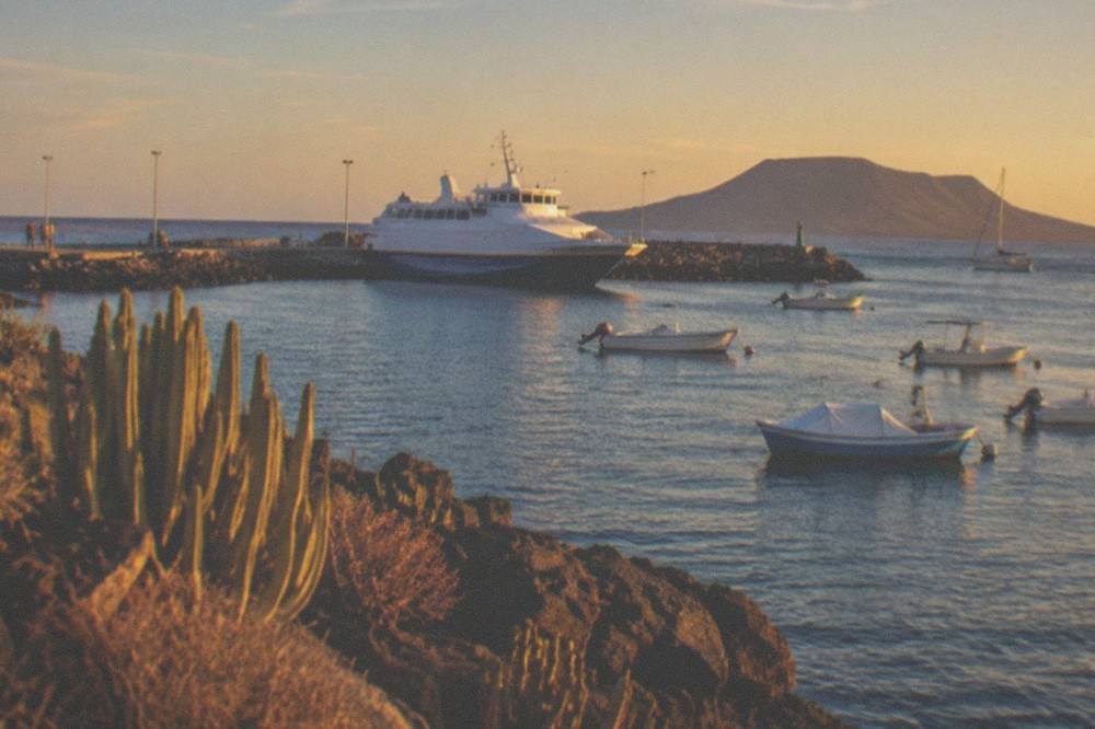 A ferry and small boats in a harbour with a volcanic island on the horizon