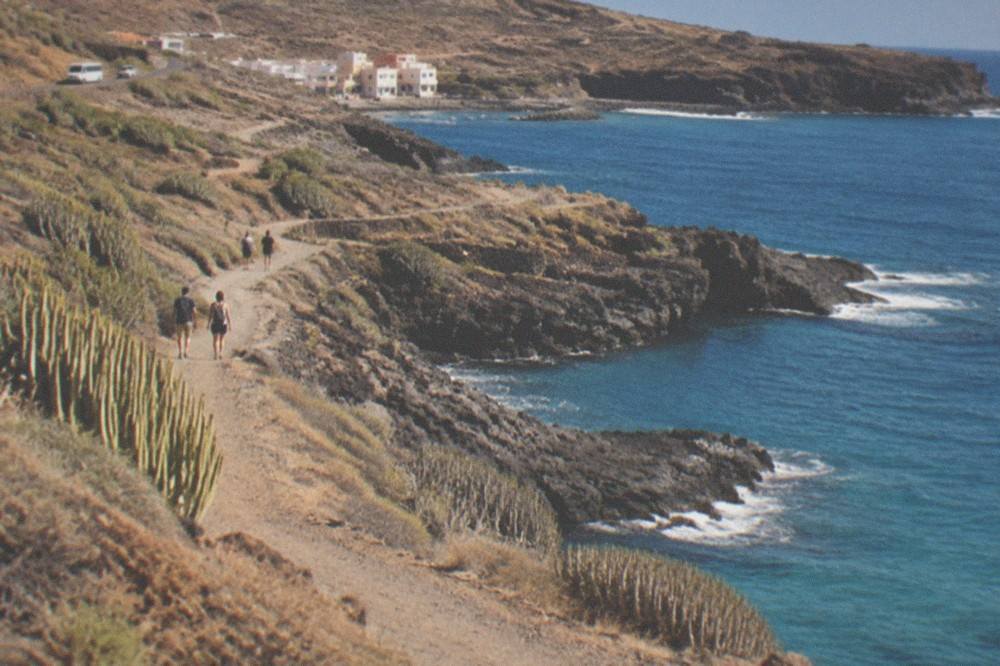 A coastal path beside calm turquoise water in late afternoon light